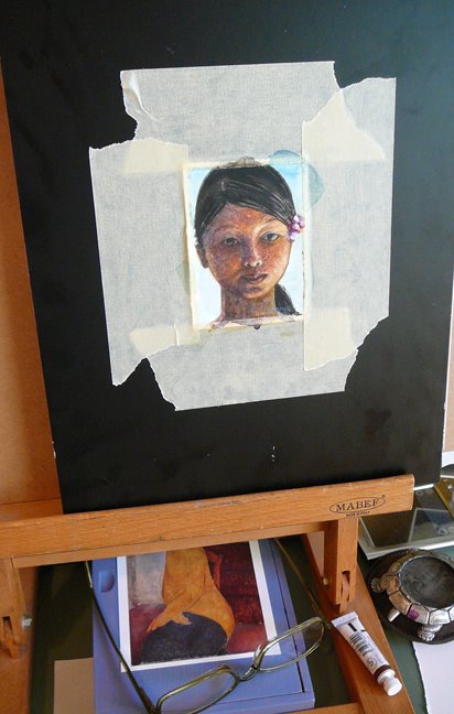 A tiny portrait of a face in watercolor, taped to a board in a studio, in process