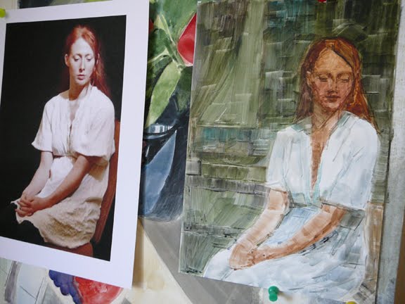 a watercolor portrait in process. next to the reference photo, in an art studio