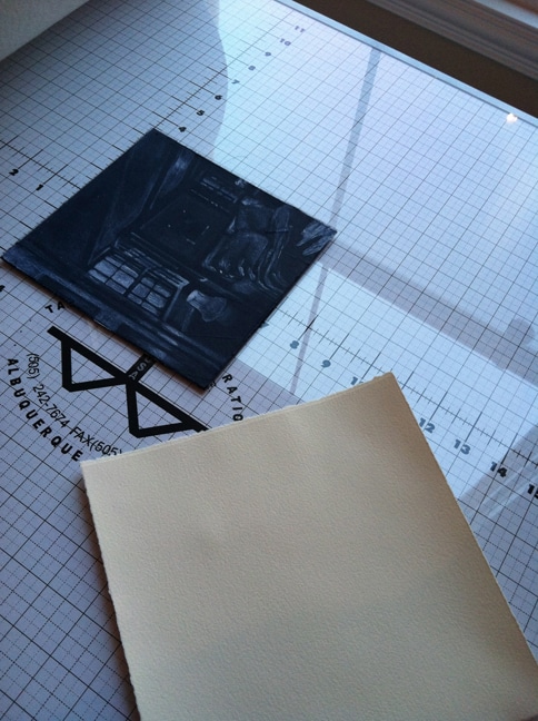 a silk aquatint plate, inked and wiped on the press bed, next to a sheet of paper, ready to print