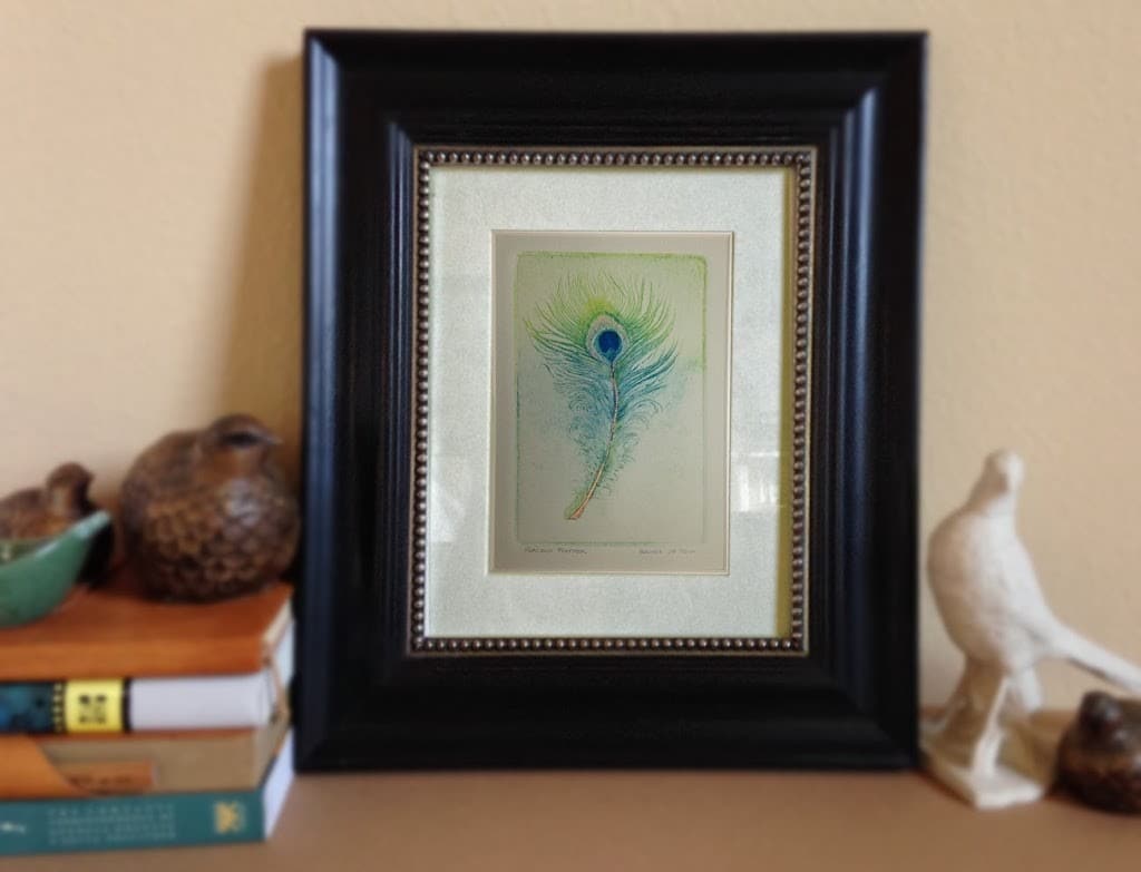 A feather from a peacock drypoint etching in turquoise and lime green with metallic copper pigments and cobalt blue, framed and ready for a wall.