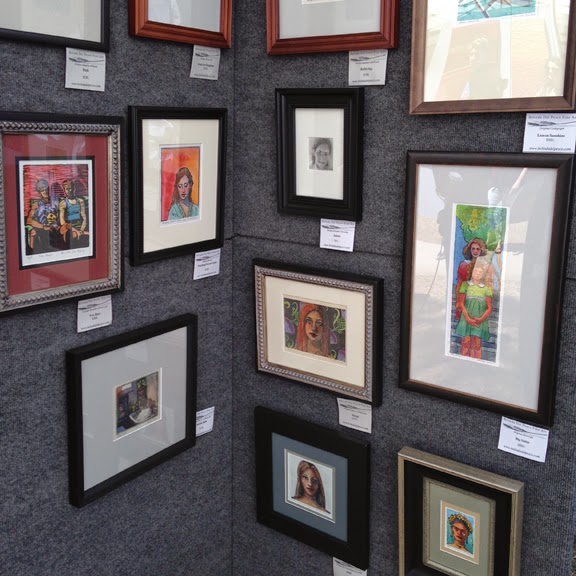 watercolors and printmaking art displayed on panels at an art festival