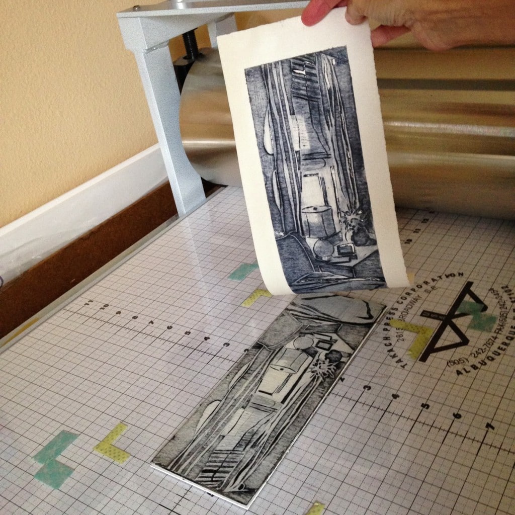 pulling a collagrapg print from an inked sheet of carved mat board after a trip through an etching press