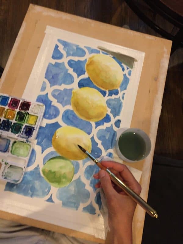 painting watercolor with a small palette and cup of water on a lap desk on the couch