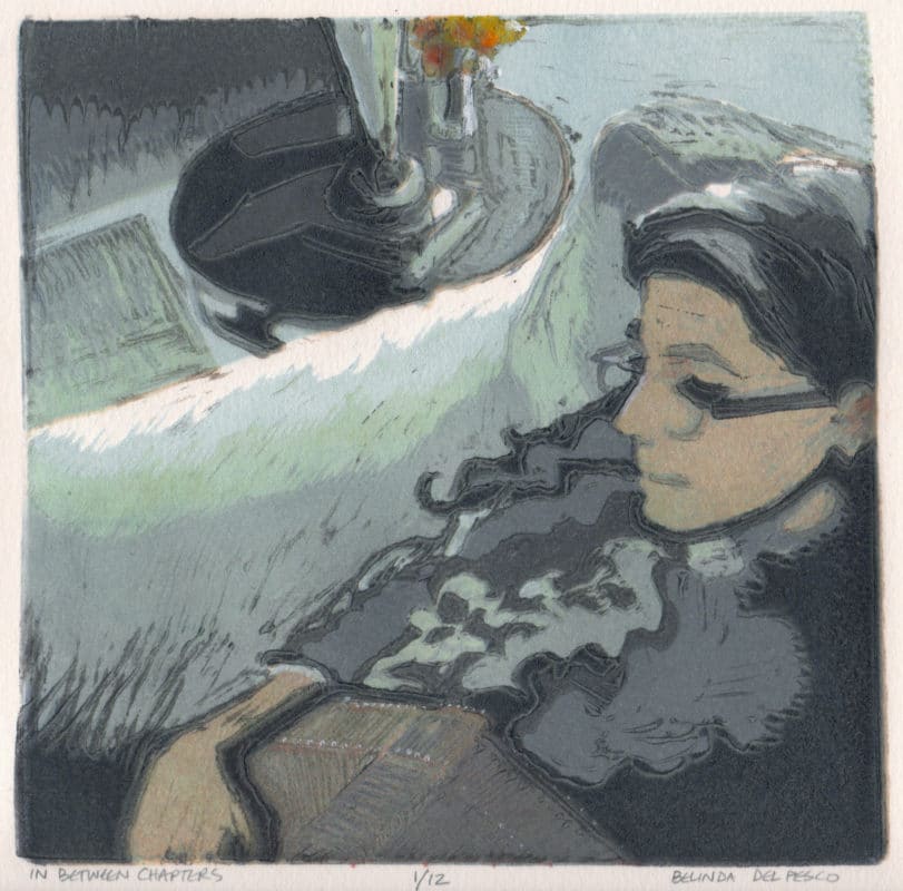 Multi-color linocut in soft colors of a woman sitting in an overstuffed chair with a book in her lap