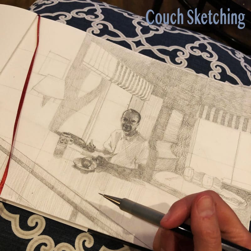 drawing in pencil of a man inside a cabin sitting at a counter, on a sketchpad propped on a pillow on my lap