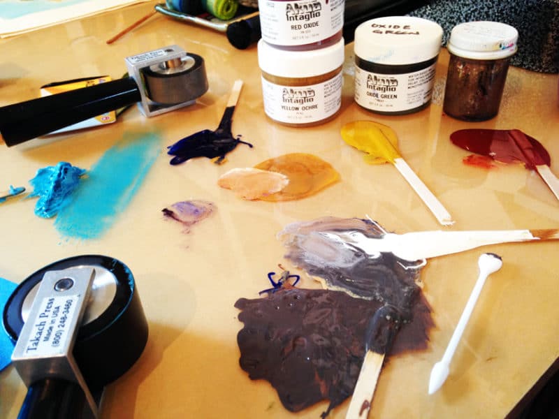 blobs of ink on a plexiglass covered work surface, with printmaking and inking tools around 